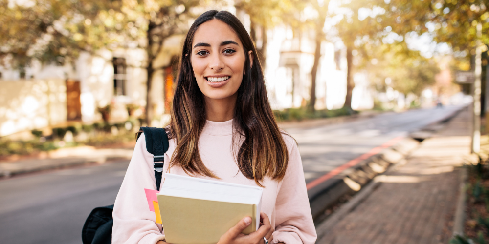 University student holding books and smiling.