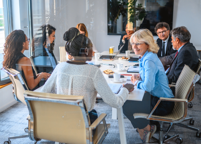 Several adults sit around a table in a board room talking.